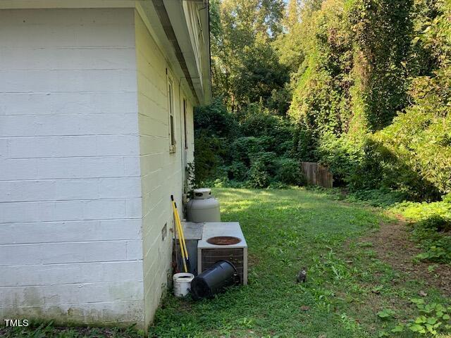 view of side of home with central AC, concrete block siding, and a yard