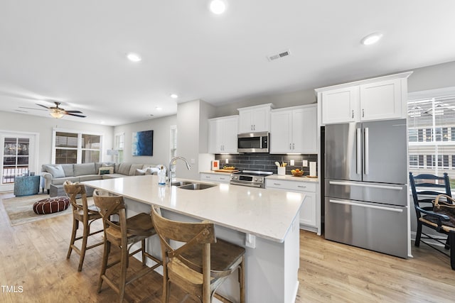 kitchen featuring a kitchen island with sink, stainless steel appliances, a kitchen breakfast bar, and white cabinets