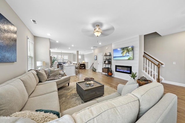 living room with light hardwood / wood-style floors, a large fireplace, and ceiling fan