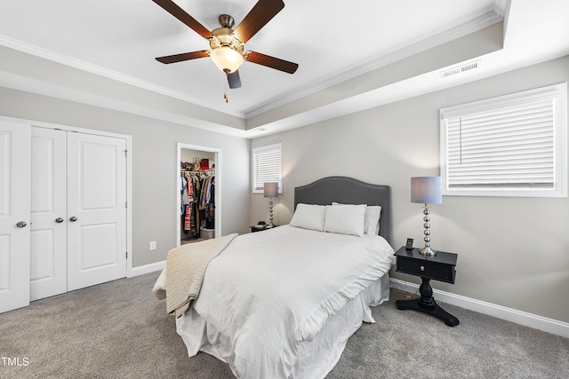 carpeted bedroom featuring ceiling fan, ornamental molding, a raised ceiling, and a walk in closet