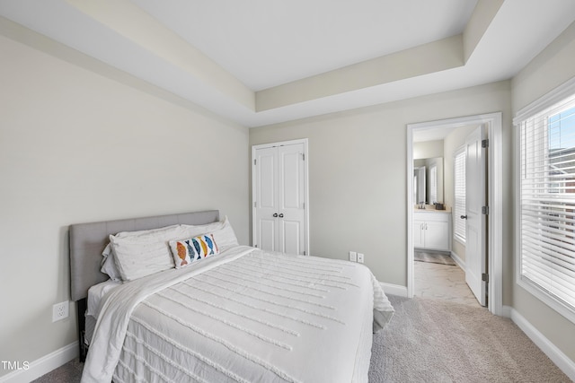 bedroom featuring a closet, connected bathroom, a raised ceiling, and light carpet