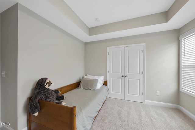 bedroom with a tray ceiling, carpet floors, and a closet