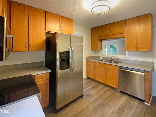 kitchen featuring a textured ceiling, appliances with stainless steel finishes, sink, and light hardwood / wood-style flooring