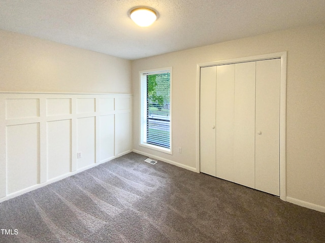 unfurnished bedroom with a textured ceiling, dark carpet, and a closet