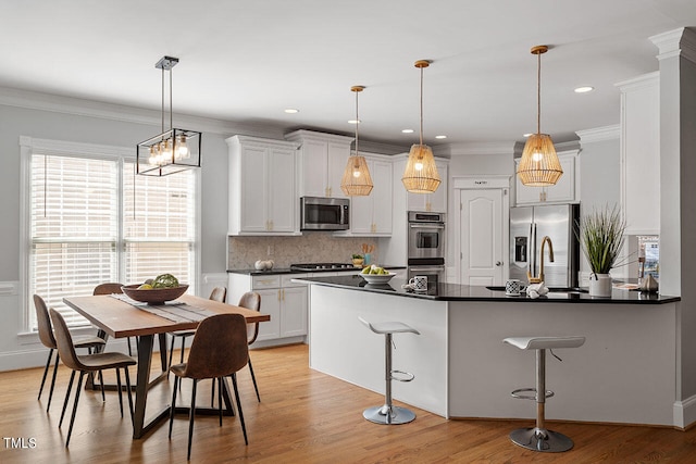 kitchen with appliances with stainless steel finishes, light wood-type flooring, a kitchen bar, and hanging light fixtures