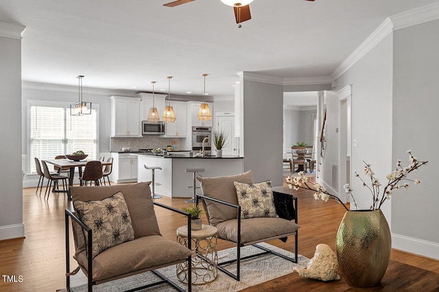 living room with ornate columns, crown molding, ceiling fan, and light hardwood / wood-style flooring