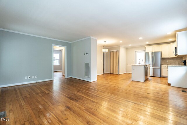 unfurnished living room featuring light hardwood / wood-style floors, ornamental molding, and sink