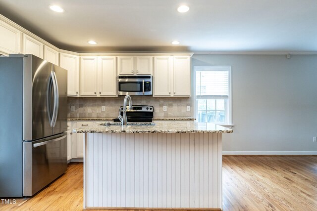 kitchen with backsplash, a center island with sink, light stone countertops, light wood-type flooring, and appliances with stainless steel finishes