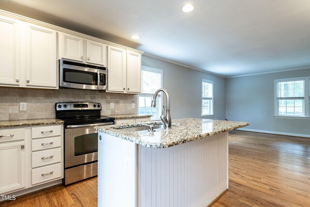 kitchen with a center island with sink, crown molding, appliances with stainless steel finishes, and light hardwood / wood-style flooring