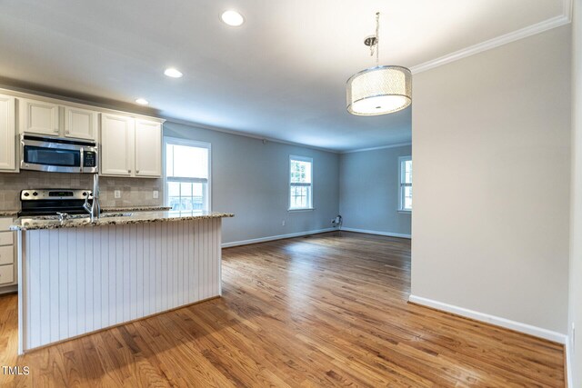 kitchen featuring backsplash, hanging light fixtures, light hardwood / wood-style floors, white cabinetry, and stainless steel appliances