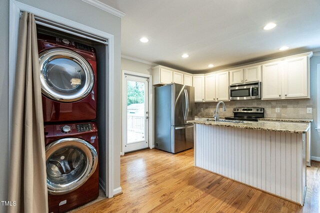 kitchen with stacked washer / dryer, a kitchen island with sink, white cabinets, and appliances with stainless steel finishes