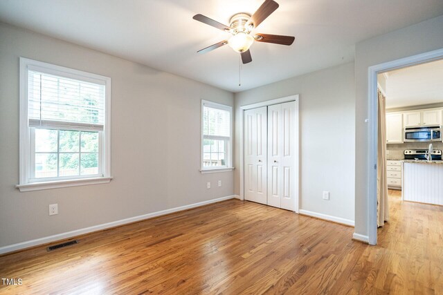 unfurnished bedroom featuring light wood-type flooring, a closet, multiple windows, and ceiling fan