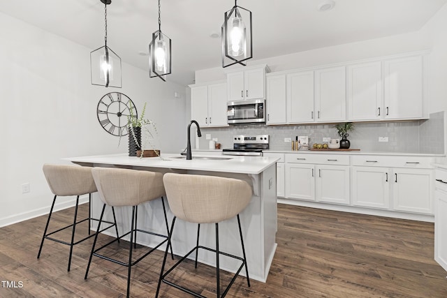 kitchen with white cabinets, appliances with stainless steel finishes, a center island with sink, and hanging light fixtures