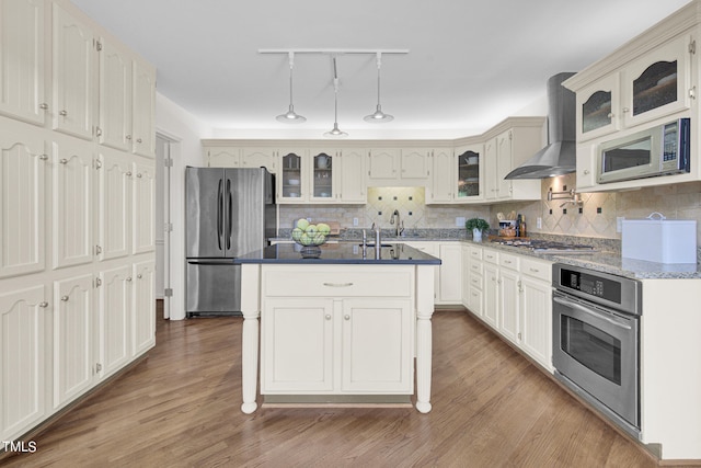 kitchen featuring stainless steel appliances, wall chimney range hood, a kitchen island, and light wood-type flooring