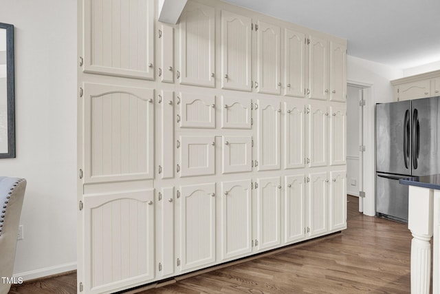 kitchen with stainless steel fridge, white cabinetry, and wood-type flooring