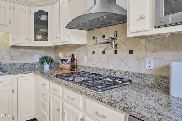 kitchen with light stone counters, tasteful backsplash, wall chimney range hood, white cabinetry, and appliances with stainless steel finishes