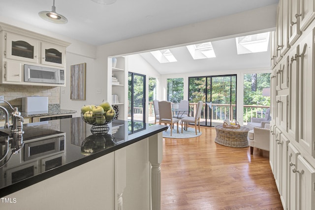 kitchen featuring lofted ceiling with skylight, tasteful backsplash, light hardwood / wood-style flooring, white microwave, and white cabinets