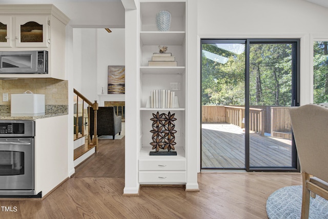 kitchen featuring light wood-type flooring, light stone countertops, stainless steel appliances, white cabinetry, and backsplash