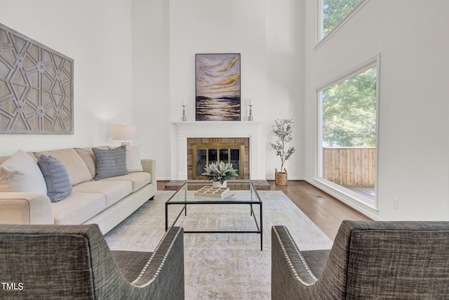 living room with hardwood / wood-style flooring, a brick fireplace, and a towering ceiling