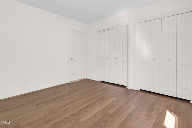 unfurnished bedroom with hardwood / wood-style flooring and multiple closets