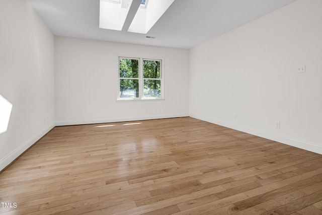 spare room with a skylight and light hardwood / wood-style flooring