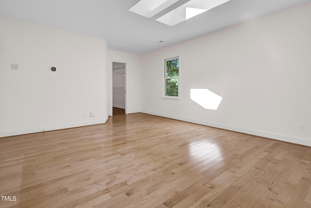 unfurnished room featuring a skylight and light hardwood / wood-style flooring