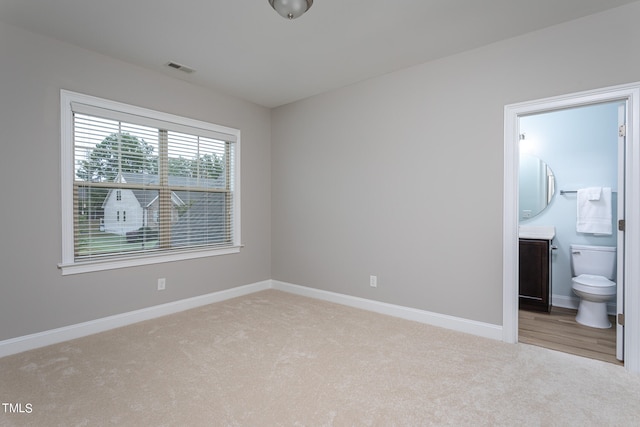 unfurnished bedroom with carpet flooring, ensuite bath, visible vents, and baseboards