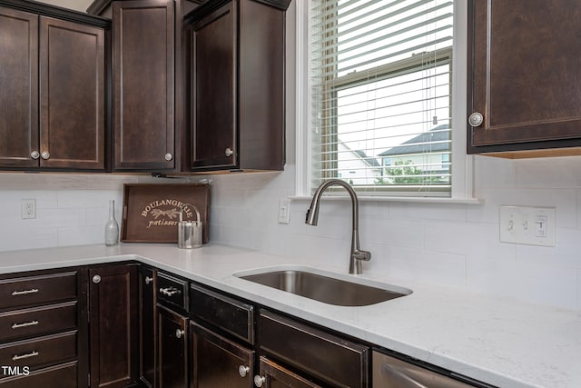 kitchen featuring decorative backsplash, light stone countertops, dark brown cabinetry, and sink