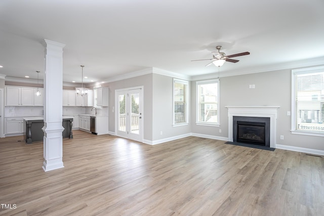 unfurnished living room with ornamental molding, a fireplace with flush hearth, light wood-style floors, and ornate columns