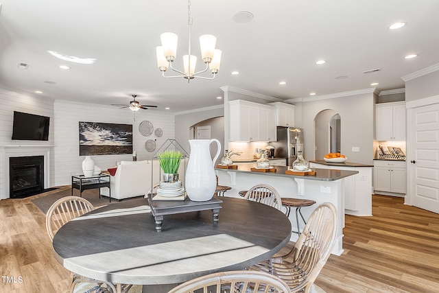 dining space featuring ceiling fan with notable chandelier, a large fireplace, light hardwood / wood-style floors, and ornamental molding