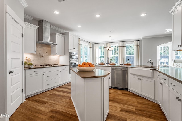 kitchen with stainless steel appliances, wall chimney range hood, hardwood / wood-style floors, white cabinetry, and sink