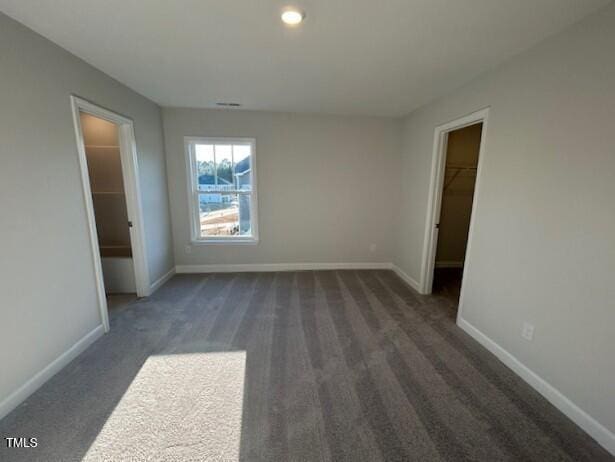 unfurnished bedroom with a closet, a spacious closet, and dark carpet