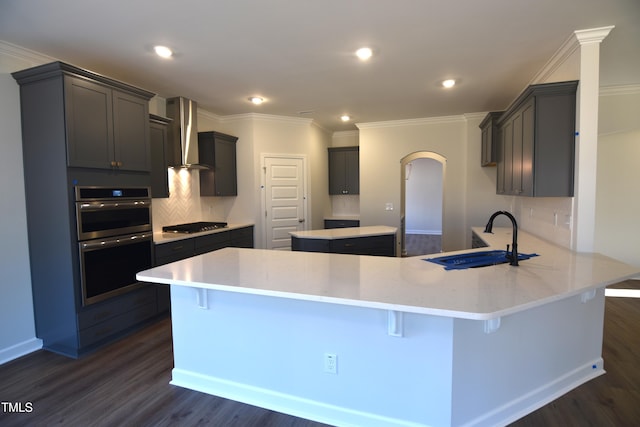 kitchen with sink, wall chimney exhaust hood, kitchen peninsula, dark hardwood / wood-style floors, and appliances with stainless steel finishes