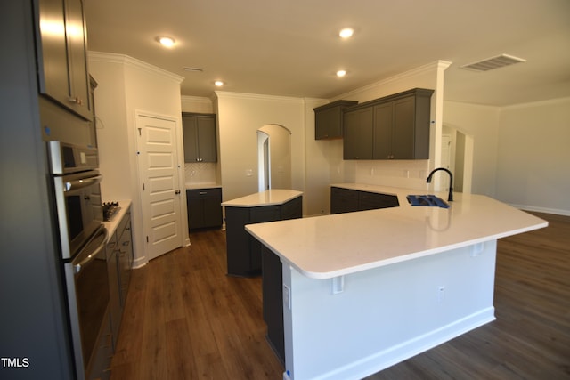 kitchen with crown molding, dark wood-type flooring, a kitchen island, sink, and tasteful backsplash