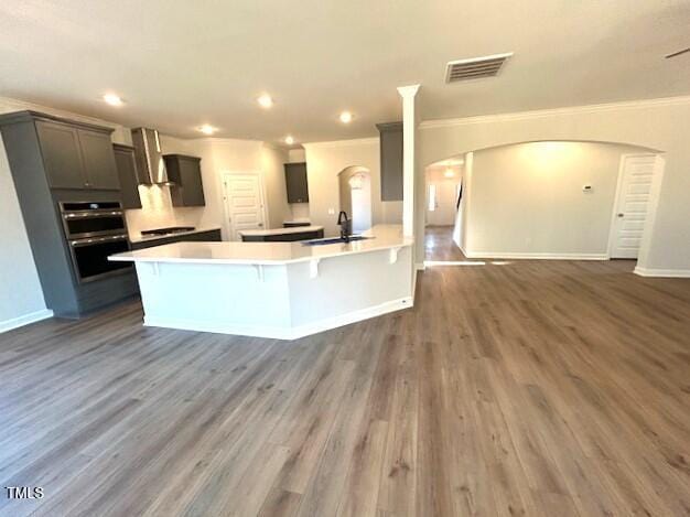 kitchen featuring a breakfast bar area, double oven, dark wood-type flooring, sink, and wall chimney range hood