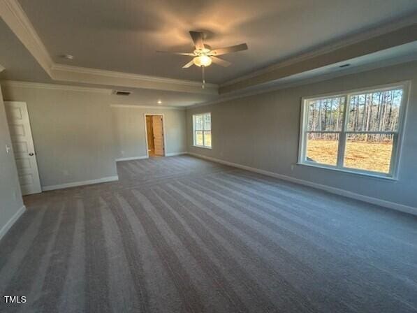 carpeted empty room with ceiling fan, a wealth of natural light, crown molding, and a tray ceiling