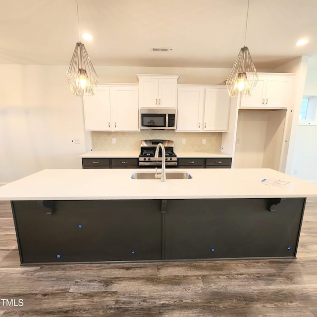 kitchen with stainless steel appliances, a center island with sink, white cabinets, and decorative light fixtures