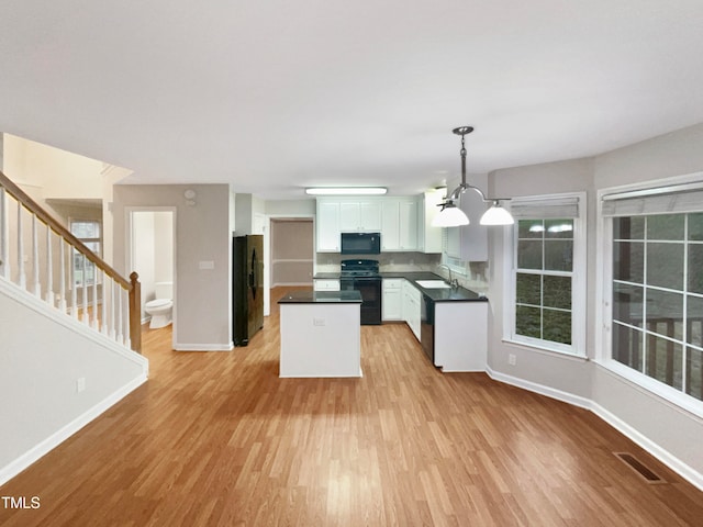 kitchen featuring light hardwood / wood-style floors, white cabinetry, pendant lighting, black appliances, and a chandelier