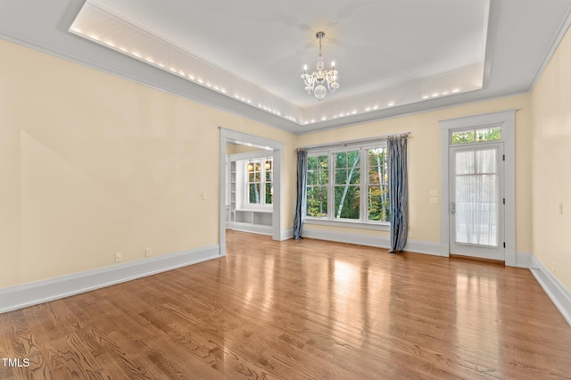 spare room with a notable chandelier, light wood-type flooring, and a tray ceiling