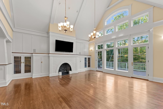 unfurnished living room featuring high vaulted ceiling, an inviting chandelier, a brick fireplace, a healthy amount of sunlight, and wood-type flooring