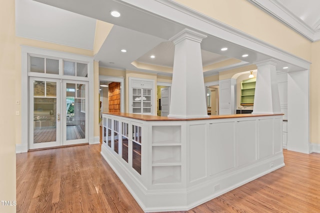 interior space with a tray ceiling, ornate columns, white cabinets, and light hardwood / wood-style floors