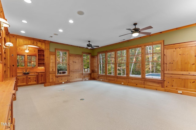 carpeted living room featuring ceiling fan, crown molding, and wooden walls