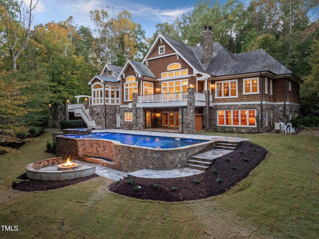 rear view of property with a balcony, an outdoor fire pit, and a lawn