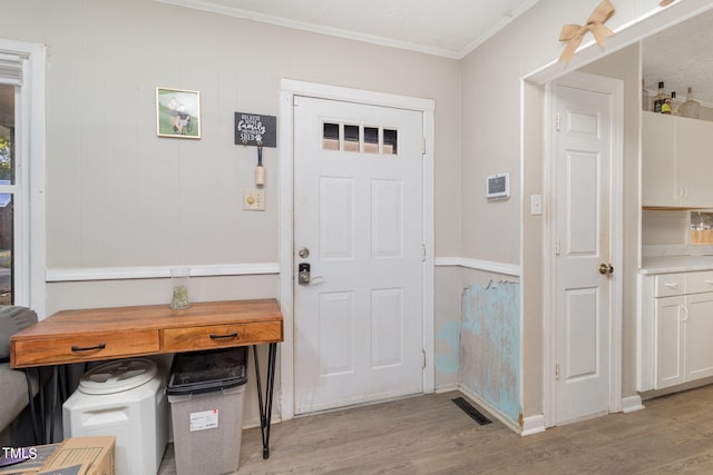 foyer with ornamental molding, light hardwood / wood-style floors, and a textured ceiling