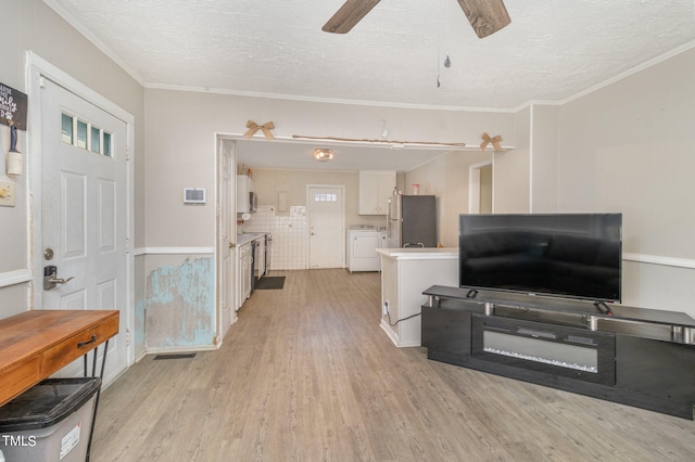 living room with light wood-type flooring, a textured ceiling, separate washer and dryer, and crown molding