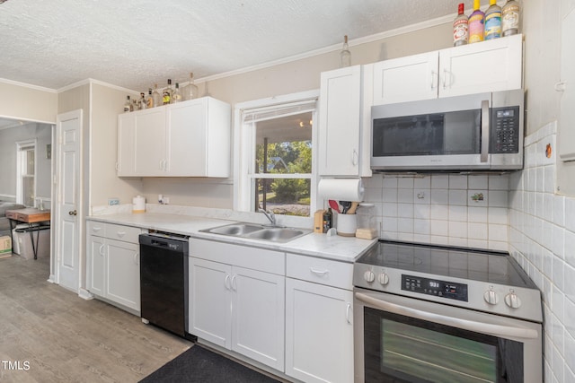 kitchen with white cabinets, ornamental molding, sink, appliances with stainless steel finishes, and light wood-type flooring