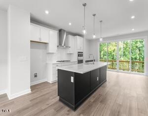 kitchen with a center island with sink, white cabinets, light hardwood / wood-style flooring, wall chimney exhaust hood, and decorative light fixtures