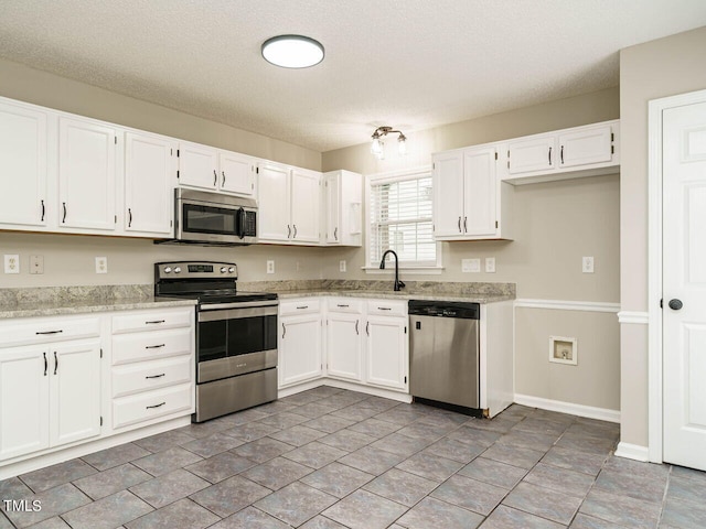 kitchen featuring appliances with stainless steel finishes, white cabinetry, light stone counters, a textured ceiling, and sink