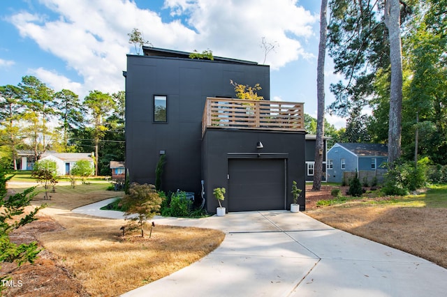 modern home featuring concrete driveway, a balcony, stucco siding, and a garage