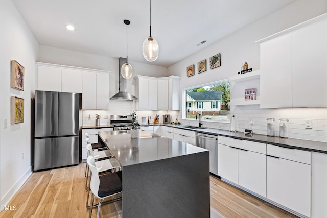 kitchen featuring wall chimney exhaust hood, light hardwood / wood-style floors, pendant lighting, white cabinets, and appliances with stainless steel finishes